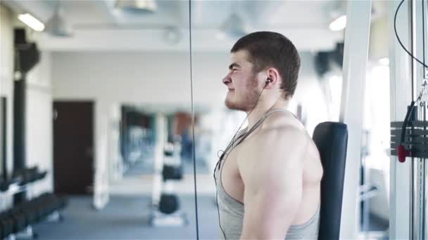 Молодий підходить чоловік тренується важко на ваговій машині тренування м'язів рук в тренажерному залі — стокове відео
