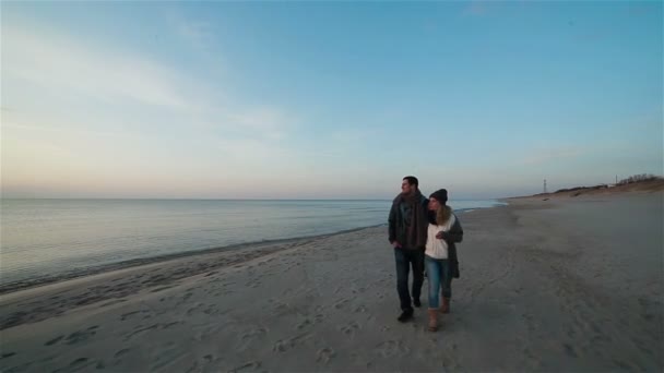 Joven hermosa pareja enamorada caminando lentamente lado a lado a lo largo de la costa en la playa con arena húmeda junto al mar, viendo la puesta de sol y hablando — Vídeos de Stock