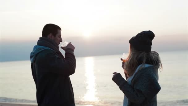 Jonge mooie verliefd paar met opwarming van de aarde drankjes en genieten van de prachtige zonsondergang zeezicht, bespreken alcohol keuze, glimlachend, hand in hand en kussen — Stockvideo