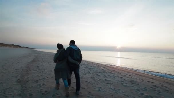 Joven hermosa pareja enamorada caminando lentamente lado a lado a lo largo de la costa en la playa con arena húmeda junto al mar, viendo la puesta de sol y hablando — Vídeo de stock