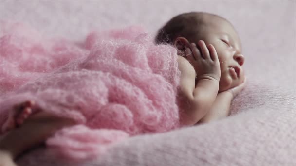 Nahaufnahme eines entzückenden kleinen neugeborenen Mädchens, das auf einer rosafarbenen Strickdecke schläft, in einer entzückenden Pose, die Hände an die Wangen gedrückt — Stockvideo