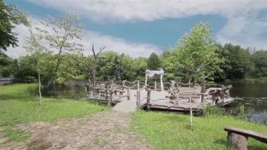 Bir düğün töreni için otantik açık ahşap yer. Sunak arch düğün beyaz kumaşlarla dekore edilmiştir. Nehir kıyısında düğün. Steadicam