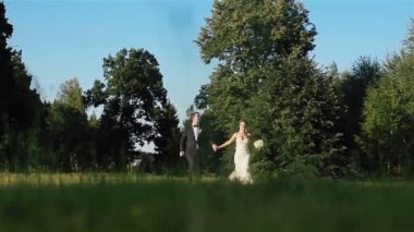 Elele ve birlikte çalışan yeşil çayır düğün gününde mutlu yeni evli çift gülümsüyor. Kamera için düz Önden Görünüm