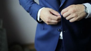 Ceketinin düğmelerini ilikliyorum. Ceketinin düğmelerini bağlayan takım elbiseli şık bir adam dışarı çıkmaya hazırlanıyor. Kapat.