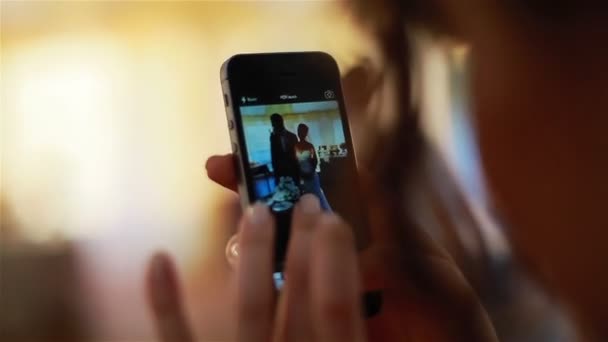 Λήψη εικόνας με ένα smartphone της νεόνυμφο ζευγάρι. Γυναικεία χέρια με περιποιημένα νύχια αφής οθόνης ενός smartphone κάνοντας την εικόνα της νύφης και ο νεόνυμφος στέκεται κοντά την γαμήλια τούρτα σε ένα εστιατόριο τραπέζι — Αρχείο Βίντεο
