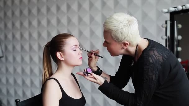 Professionele make-up artiest toepassing van oogschaduw aan modellen ooglid. Make-up in een schoonheidssalon. Stijlvolle mensen werken. Middellange schot — Stockvideo