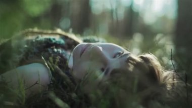 Ormandaki genç kadın yosunların üzerinde uzanıyor ve etrafındaki bitkilere dokunuyor. Kapat.
