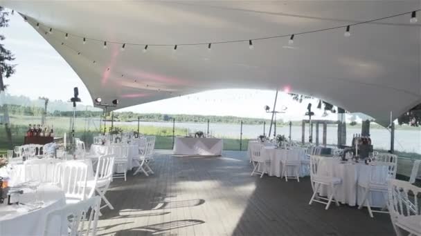 Everything is set and ready for the wedding party in an outdoor restaurant. Wedding reception decoration with all white on summer terrace near the lake. Flycam — Stock Video