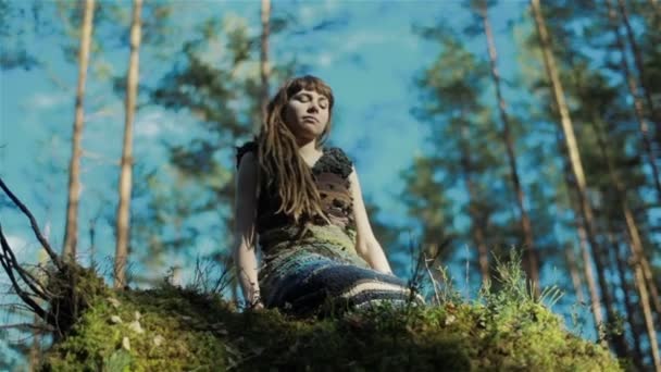 Jonge vrouw in het bos zittend op een mossige heuvel en aangrijpende planten om haar heen. Sluiten. — Stockvideo