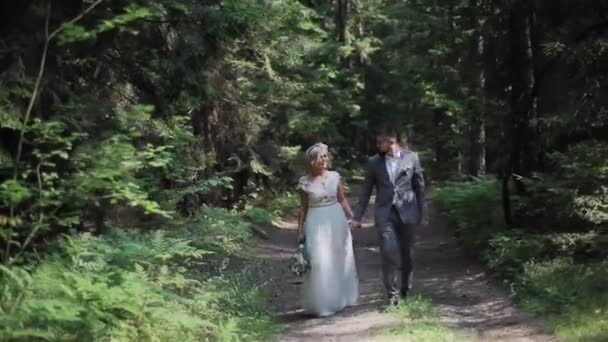 Fiatal és boldog menyasszony és vőlegény sétálnak a napfényes erdőben — Stock videók