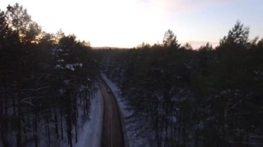 4K aerial flying view from above. Following patched forest road with moving cars and flying into sunlit industrial city suburb valley landscape with epic sunset view
