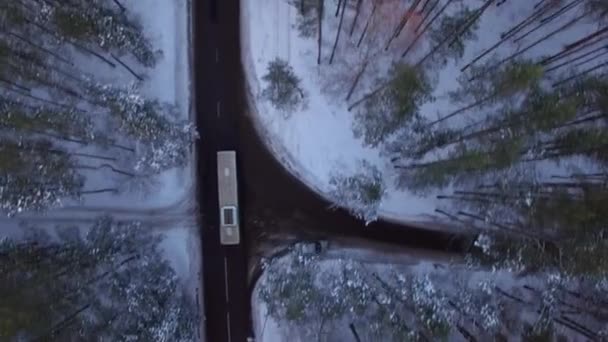 Vista aérea de 4K desde arriba. Siguiendo el autobús local que se mueve en la carretera forestal de invierno con copas de árboles de nieve al atardecer o al amanecer — Vídeos de Stock