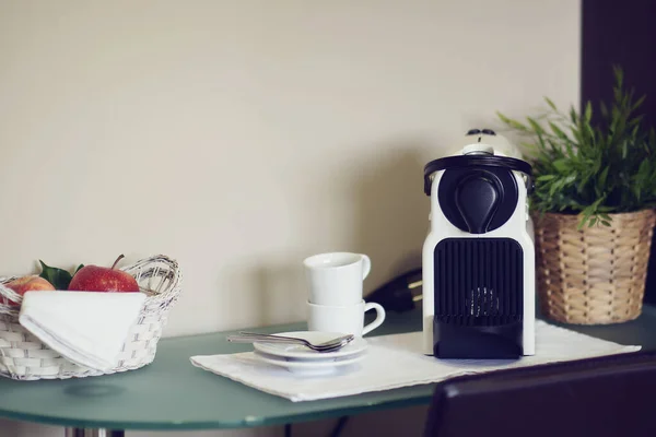 Kahvaltı için hazır kahve makinesi, fincanlar, kaşıklar ve meyve sepetiyle.