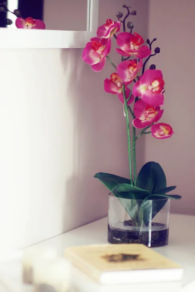 Güzel pembe bir orkide tenceresi ve bir kitabı olan bir tuvalet masası.