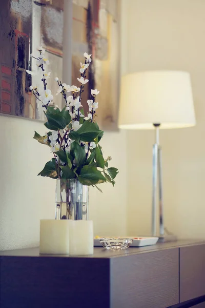 Komodinin yanında pembe çiçekli vazo ve kitapla süslenmiş..