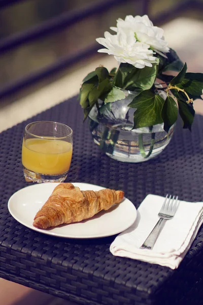 Terasta kahvaltı var. Doğal portakal suyu ve kruvasanla birlikte bahçe masası. Bir vazo beyaz çiçekle süslenmiş..