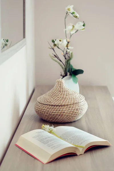 Komodinin yanında pembe çiçekli vazo ve kitapla süslenmiş..