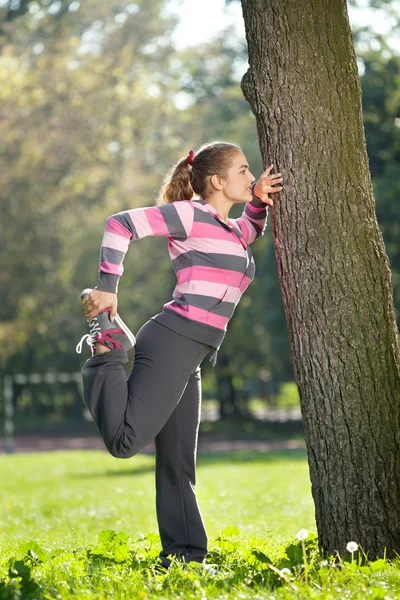 Joven hermosa mujer estirando su pierna en el parque de la ciudad —  Fotos de Stock