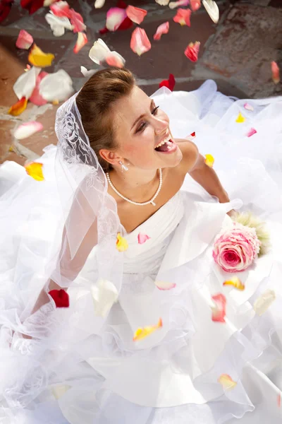 Felice sposa ridente seduta all'aperto sul pavimento con petali — Foto Stock
