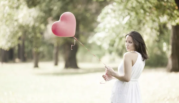 Triste jovem mulher de pé com um balão de coração em forma de vermelho — Fotografia de Stock