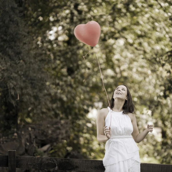 Jovem sorridente feliz com um balão de coração em forma de vermelho — Fotografia de Stock