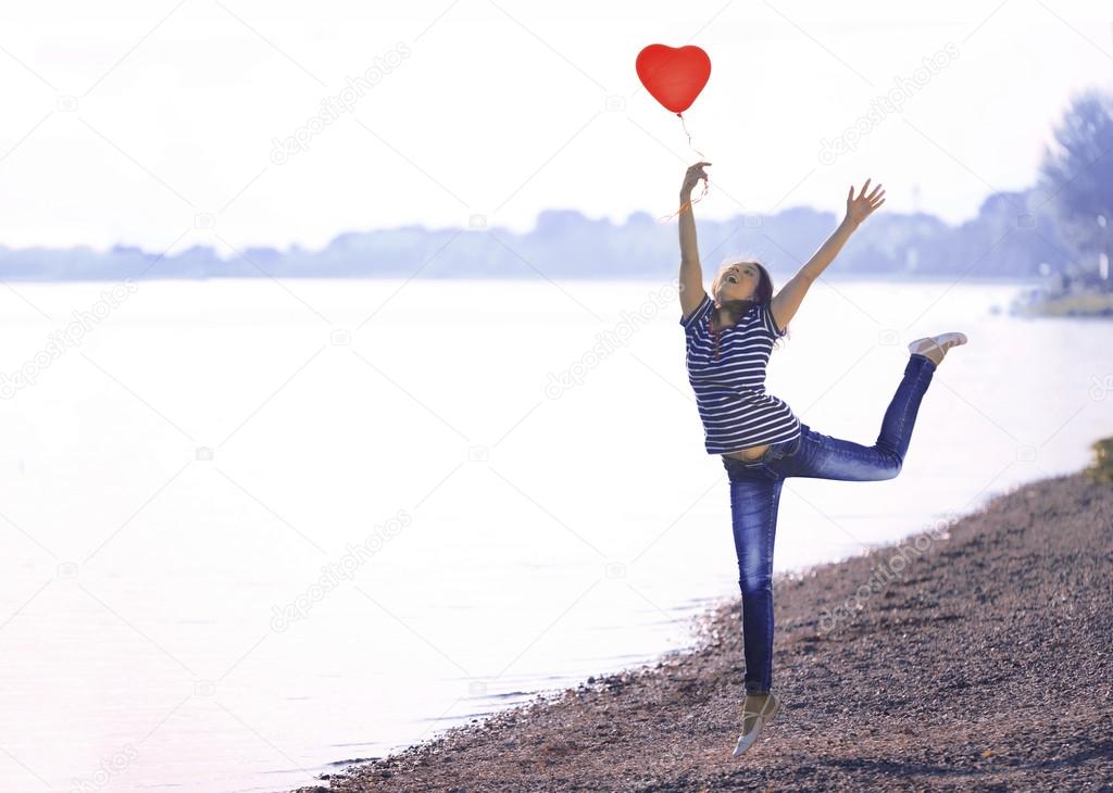 Happy Young Woman Jumping with a Shaped Heart Balloon