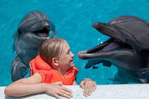 Niña feliz riéndose con dos delfines en la piscina — Foto de Stock