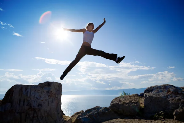 Beautiful young woman jumping from the rock — Stock Photo, Image