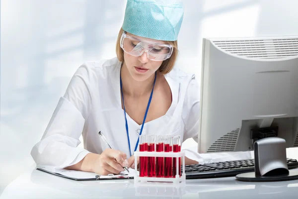 Young woman scientist examining a test tube with red liquid — Stock Photo, Image