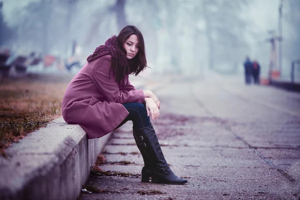 Traurige junge Frau sitzt draußen — Stockfoto