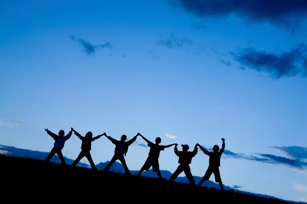 Silhouetten von sechs Kindern, die gemeinsam in den blauen Himmel springen — Stockfoto