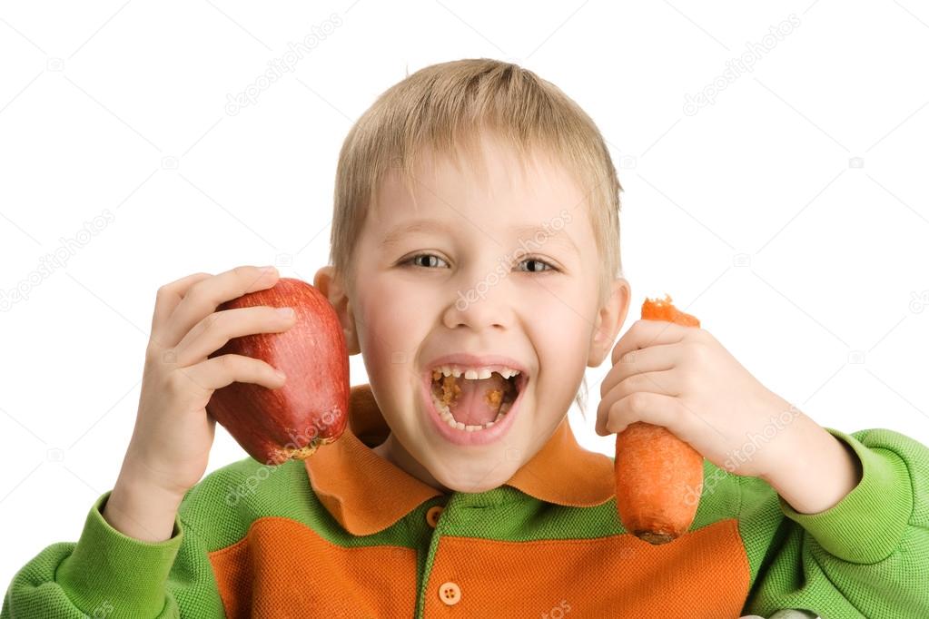 Happy little boy biting apple and carrot