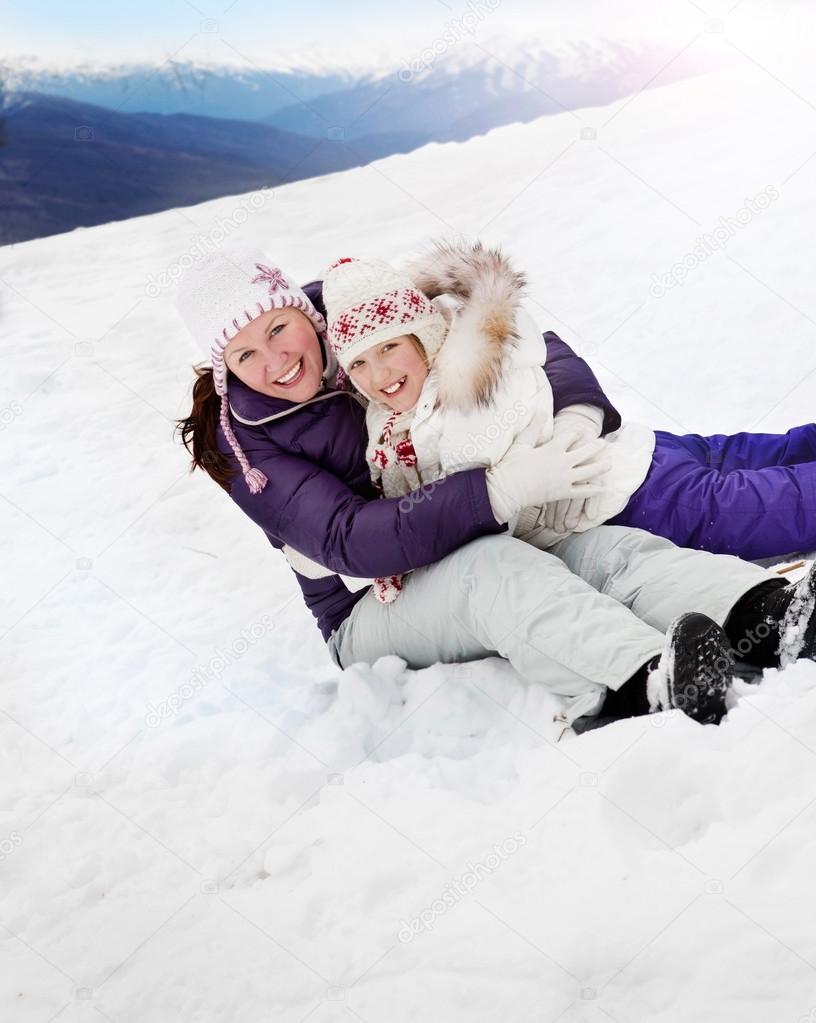 Happy Mother and Daughter Sitting on the Snow in Mountains
