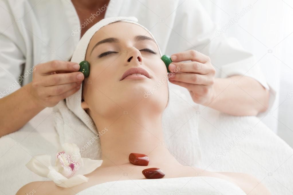 Spa salon: Young Beautiful Woman Having Facial Massage with Ston