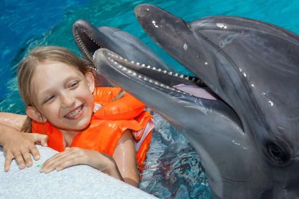 Glückliches kleines Mädchen lacht mit zwei Delfinen im Schwimmbad — Stockfoto