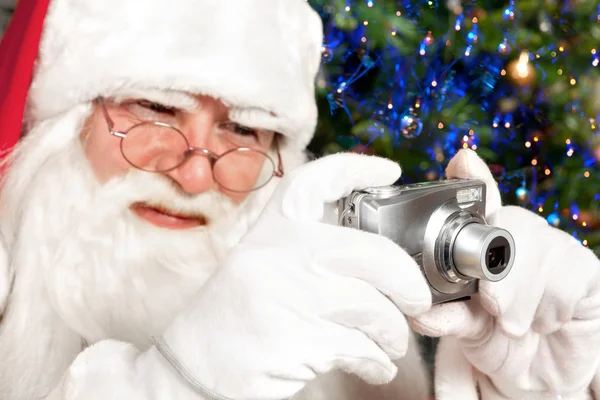 Санта-Клаус снимает на цифровую камеру рождественскую елку на заднем плане — стоковое фото