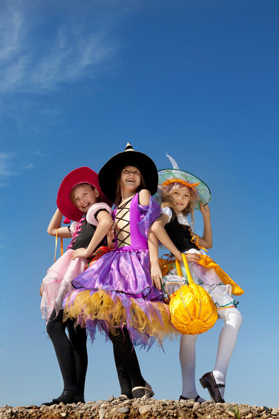 Three Cute Little Witches Standing Against the Blue Sky