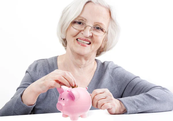 Старшая женщина экономит деньги в копилке свиньи — стоковое фото