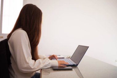 Evde bilgisayarla çalışan mutlu ve serbest bir genç kadın. İnternette okuyan çekici bir iş kadını, dizüstü bilgisayar, internet sörfü bilgisi veya internet mağazasından alışveriş yapıyor. Genç kahverengi saçlı kadın online alışveriş yapıyor..