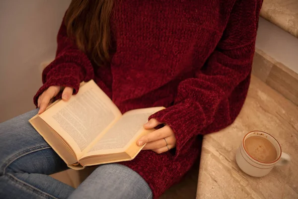Güzel genç bir bayan kitap okuyor ve mutlu bir şekilde kahve içiyor. Uzun kahverengi saçlı bir kadın kitap okuyor. Merdivenlerde oturan kadın..