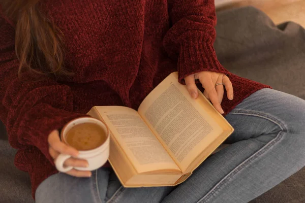 pretty young woman reading a book and drinking coffee happily. Woman with long brown hair reading a book. Woman sitting on some stairs.
