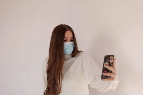 Kendini COVID-19 'dan korumak için maske takan genç bir kadın ve beyaz arka planda izole edilmiş bir şekilde baş parmağını kaldırıyor. Önünde eli olan genç bir kadın. Telefonu kullanan genç bir kadın. Genç bir kadın video görüşmesi yapıyor.