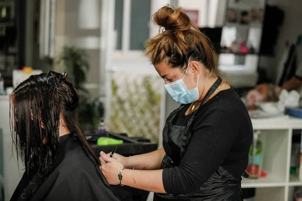 Woman with face mask getting a fresh style at a hair salon. Woman getting a hair wash. Hairdressing concept. Hairdresser cutting and styling a woman in her shop