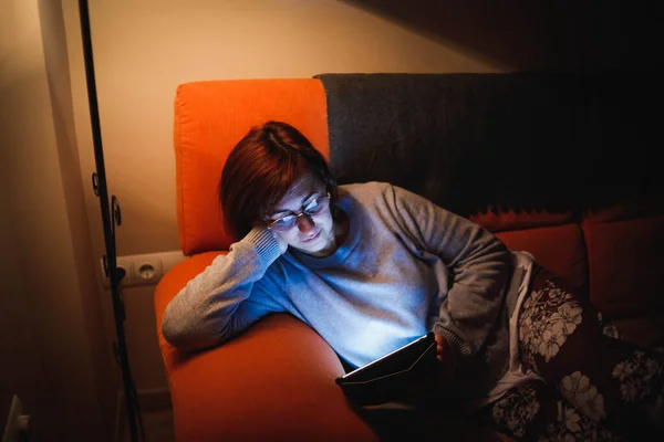 Oturma odasında dokunmatik tablet kullanan yetişkin bir kadın. Yetişkin bir kadın dokunmatik bir cihaz kullanıyor. Kitap okuyan bir kadın. Ailesiyle video görüşmesi yapan bir kadın.