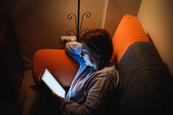 adult woman using a touch tablet in the living room. Adult woman using a touch device. Woman reading a book. Woman making video call with family