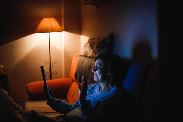 adult woman using a touch tablet in the living room. Adult woman using a touch device. Woman reading a book. Woman making video call with family