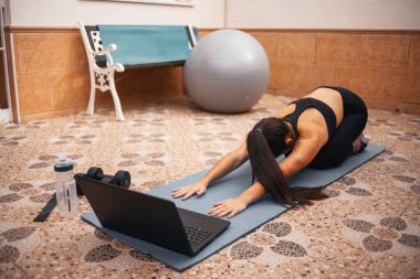 Evde dizüstü bilgisayarla egzersiz yapan bir kadın. Sağlıklı kadın yoga tahtası yapıyor ve dizüstü bilgisayardan online dersler izliyor.
