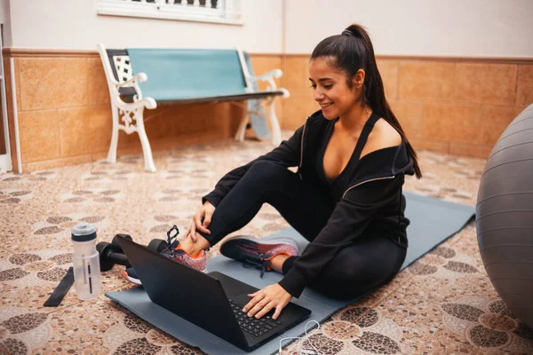 Evde dizüstü bilgisayarla egzersiz yapan bir kadın. Sağlıklı kadın yoga tahtası yapıyor ve dizüstü bilgisayardan online dersler izliyor.
