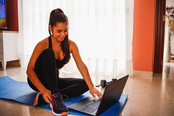 Evde dizüstü bilgisayarla egzersiz yapan bir kadın. Sağlıklı kadın yoga tahtası yapıyor ve dizüstü bilgisayardan online dersler izliyor.