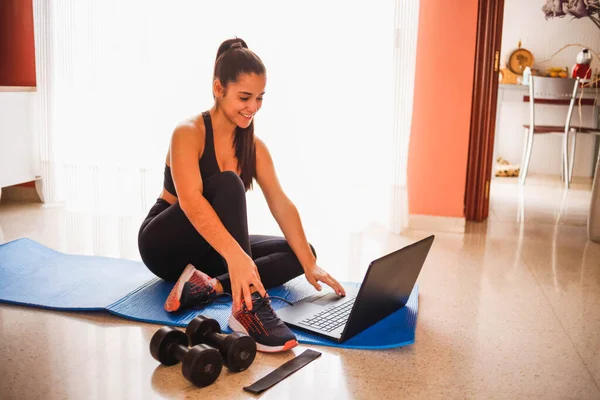 Evde dizüstü bilgisayarla egzersiz yapan bir kadın. Sağlıklı kadın yoga tahtası yapıyor ve dizüstü bilgisayardan online dersler izliyor.